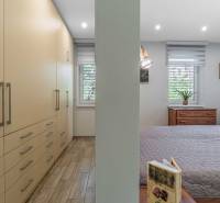 Bedroom in a family house with a bed, wardrobes, a sofa set, and windows with blinds.