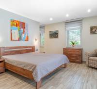 Bedroom in a family house with a bed, armchair, dresser, abstract painting, and wooden decor flooring.