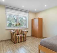 A room in a family house with an armchair, a bed, a wardrobe, and flowers on the windowsill.