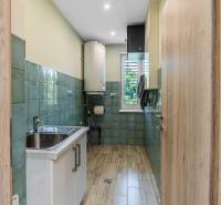 A narrow kitchen in a family house with a stainless steel sink and green tiles.