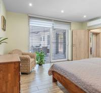 Bedroom with large doors, an armchair, a dresser, and a plant in a family house.