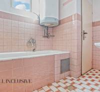 A bathroom in a family house with pink tiles and a bathtub located under the window.