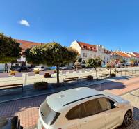 The center of Svätý Jur on Prostredná Street with cars and trees, historic houses in the background.