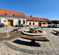 The fountain with benches on Prostredná Street in Svätý Jur, lined with historic buildings.