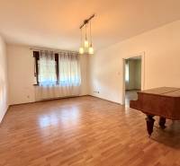 A room in a family house with a wooden decor floor, curtains, and a piano.