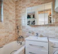 Bathroom with a bathtub, sink, and mirror in a family house, tiled with beige tiles.