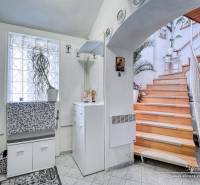 A cottage with a wooden staircase, white furniture, and a plant; interior with a wood-decor floor.