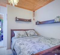 Bedroom in a cabin with a wooden ceiling, flowers, and shelves above the bed.