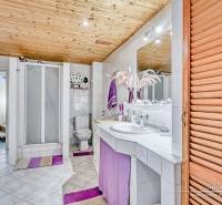 Bathroom in a family house with tiles, a shower corner, a toilet, and a wooden ceiling.