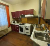 A kitchen in a family house with a wood-patterned floor, red cabinets, and white appliances.
