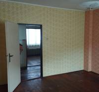 A family house with a wooden decor floor and wallpapered walls, doors leading to another room.