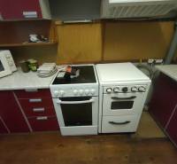 A kitchen in a family house with an oven, a cooktop, a microwave, and a floor with a wooden decor.
