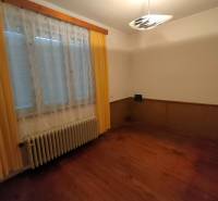 A room in a family house with a wooden decor floor, curtains, and a radiator.
