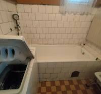 A bathroom in a family house with a bathtub and a washing machine, tiled with white tiles.