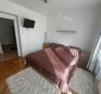 A bedroom in a three-room apartment with a wooden decor floor, a bed, and a television.