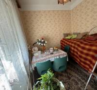 Interior of a family house with flowers, a table, and a bed with a carpet.