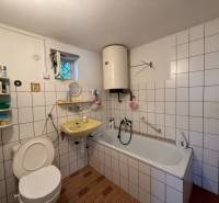 A bathroom in a family house with a bathtub, a yellow sink, tiles, and a boiler on the wall.