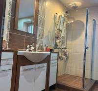 Bathroom of a 2-room apartment with a shower, sink, and cabinets.