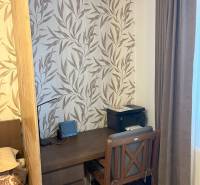 A workspace in a 2-room apartment with leaf-patterned wallpaper and dark furniture.