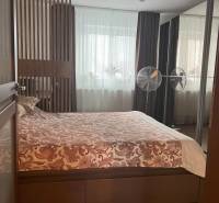 Bedroom in a two-room apartment with a double bed, lamp, and windows with heavy curtains.