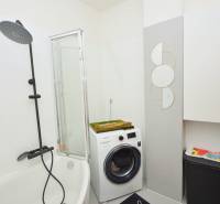 A bathroom in a 3-room apartment with a bathtub, washing machine, and a modern shower enclosure.