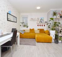 Living room with a mustard couch, white table, and wood-patterned floor, 3-room apartment.