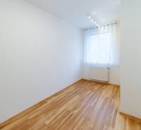 A room in a 3-room apartment with a wooden decor floor, doors, and a window with curtains.