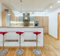 A kitchen with a bar counter and three red stools in a three-room apartment, with a wooden decor floor.