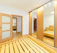 Bedroom in a 3-room apartment with wood-patterned flooring, a mirrored wardrobe, and a bed.
