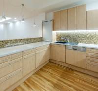 A kitchen in a 3-room apartment with wooden decor and a stone wall, well-lit by light fixtures.