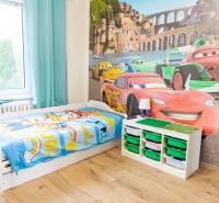 Children's room with car-themed wallpaper, a bed, and storage boxes, wooden decor flooring.