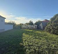 A plot for housing in Kameničná with a grassy area and neighboring houses in the background.