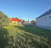 Plots - housing in Kameničná with greenery and a neighboring house under the blue sky.