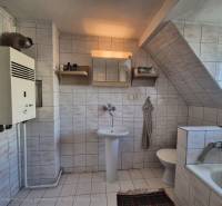 A bathroom in a family house with a bathtub, a sink, a gas boiler, and white tiles.