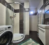 A bathroom in a family house with a washing machine, shower, and sink.