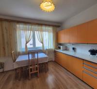 The kitchen in the family house has orange cabinets and a floor with a wood design.