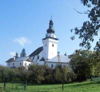 A church in Dubové surrounded by trees under a blue sky on a hillside.