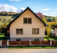 A family house in Medzev with a pyramidal roof, a fenced yard with a lawn, autumn landscape.