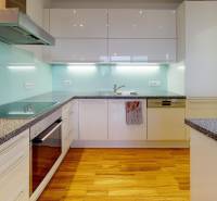 A spacious kitchen with glossy white cabinets, appliances, and a wooden decor floor in a 2-room apartment.