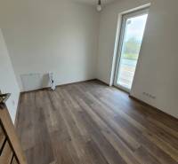 A room in a family house with a wooden-patterned floor and a large window.