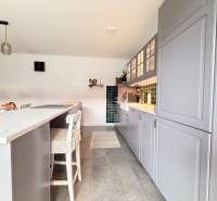 A kitchen in a family house with an island, gray cabinets, and green tiles.