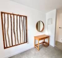 In the interior of a family house, a wall is decorated with a frame with branches, a table, and a mirror.