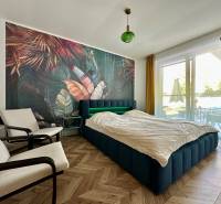 A bedroom with rich wallpaper, a wooden decor floor, a large window with a view.