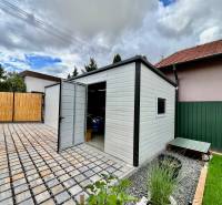 A family house in Trnava with an outbuilding and a wrought iron gate on a paved courtyard.