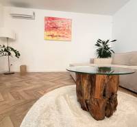 Living room with a sofa, wooden and glass table, plants, and a floor with a wooden decor.