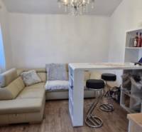 Living room in a 2-room apartment with a sofa, bar stools, and a wooden decor floor.