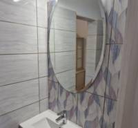 Compact bathroom in a 2-room apartment with an oval mirror and a floor with a wooden decor.