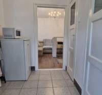 A corridor with tiles leading into a room with a wooden decor floor in a 2-room apartment.