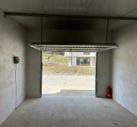 The interior of the garage has a white wall, concrete floor, and open doors.