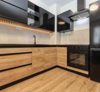 A kitchen in a 2-room apartment with a black appliance and a wooden decor floor.